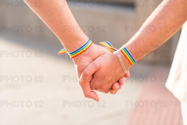 Detail of the holding hands of a couple of homosexual men with the rainbow flag at the pride party in the city