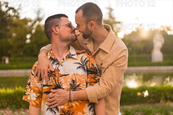Homosexual couple embracing giving each other a kiss looking at the sunset in a park in the city