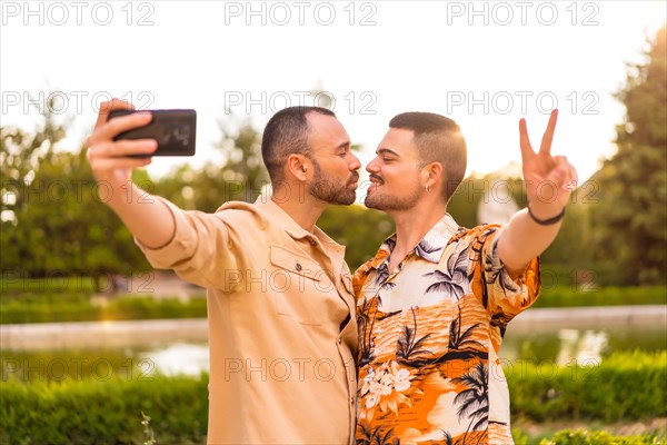 Homosexual couple taking a selfie and kissing at sunset in a park in the city