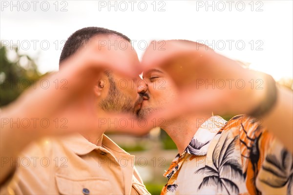 Portrait of gay boyfriend and girlfriend making the heart or love gesture kissing at sunset in a park in the city