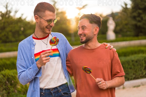 Portrait of gay boyfriend and girlfriend eating a lollipop in the park on sunset in the city
