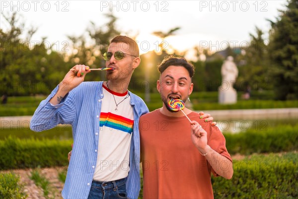 Portrait of laughing wedding couple eating a lollipop in the park on sunset in the city