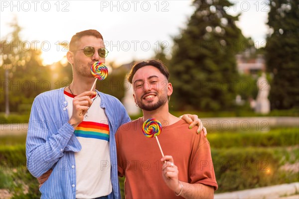 Portrait of laughing wedding couple eating a lollipop in the park on sunset in the city
