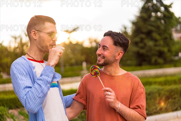 Portrait of smiling wedding couple eating a lollipop in the park on sunset in the city