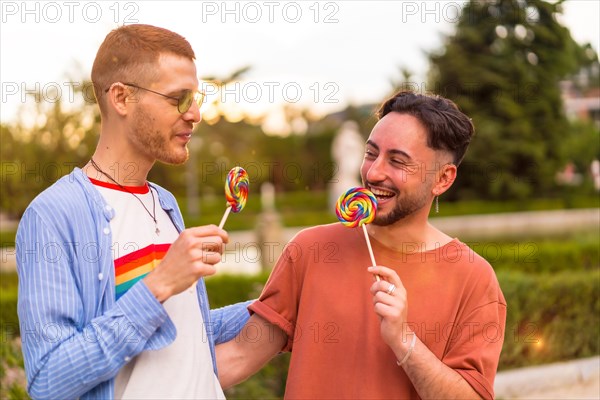 Portrait of smiling wedding couple eating a lollipop in the park on sunset in the city