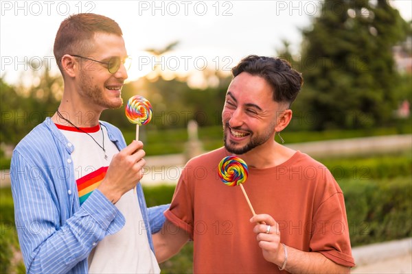 Portrait of smiling wedding couple eating a lollipop in the park on sunset in the city