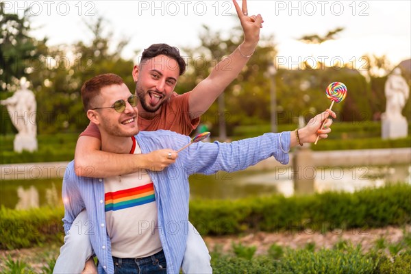 Gay boyfriends playing and one climbed on the back running eating a lollipop in the park on sunset in the city