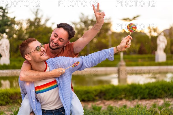 Gay boyfriends playing and one climbed on the back running eating a lollipop in the park on sunset in the city