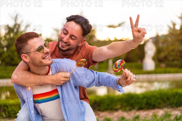 Portrait of gay boyfriend playing and one climbed on his back running eating a lollipop in the park on sunset in the city