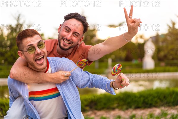 Portrait of gay boyfriend playing and one climbed on his back running eating a lollipop in the park on sunset in the city