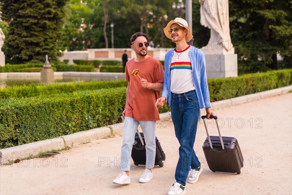 Male tourists gay boyfriends with a suitcase in the park on sunset in the city visiting the city for the pride festival