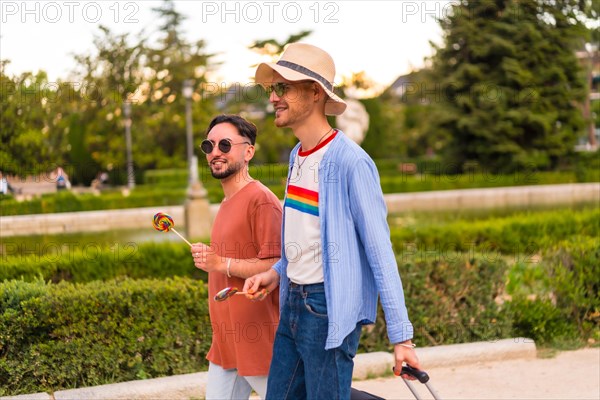 Male tourists gay boyfriends with a suitcase in the park on sunset in the city visiting the city for the pride festival