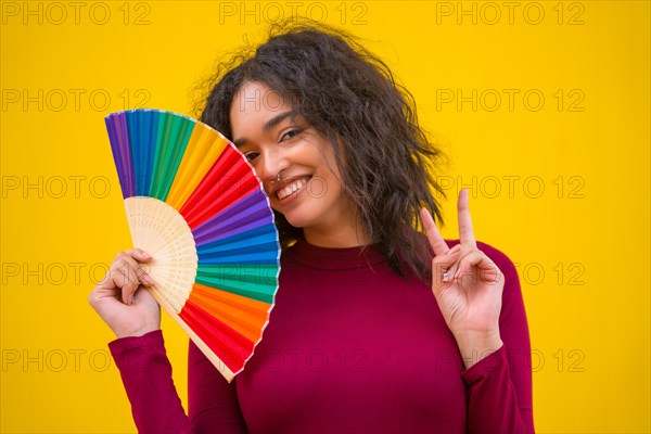 Portrait of a latin woman smiling with a rainbow lgbt fan on a yellow background