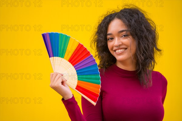 Portrait of a latin woman with a rainbow lgbt fan on a yellow background