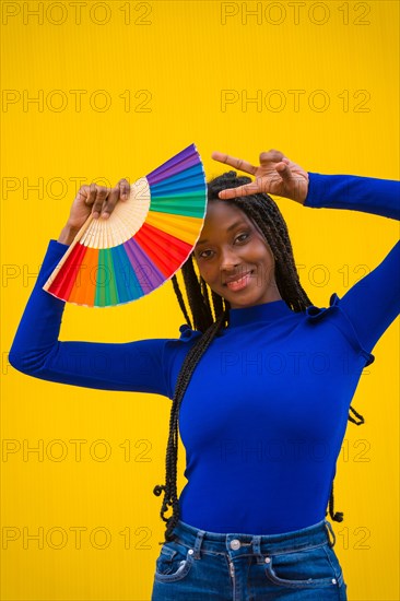 Portrait of a black ethnic woman with a rainbow lgbt fan on a yellow background