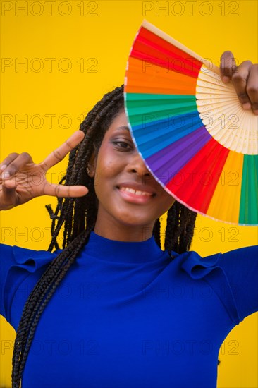 A black ethnic woman with a rainbow lgbt fan on a yellow background