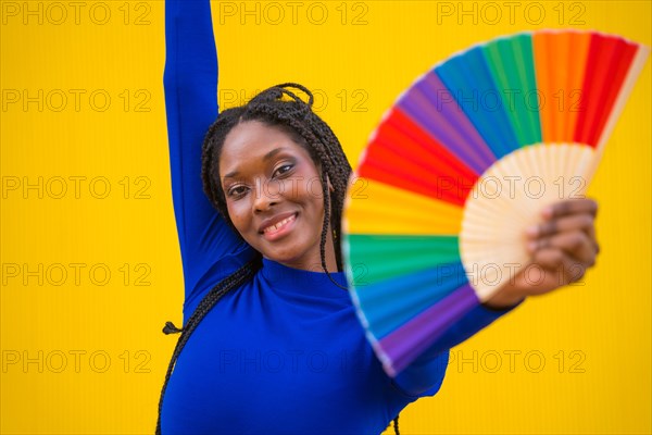 Portrait of an attractive black ethnic woman with a rainbow lgbt fan on a yellow background