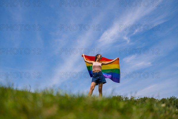 Caucasian brunette woman with a rainbow lgbt flag on the grass smiling