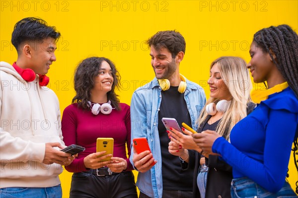 Low angle view of a group of smiling young multi ethnic teenage friends using cell phones on a yellow background