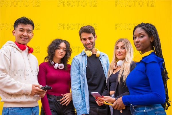 Portrait of a group of smiling young multi-ethnic teenage friends using cell phones on a yellow background