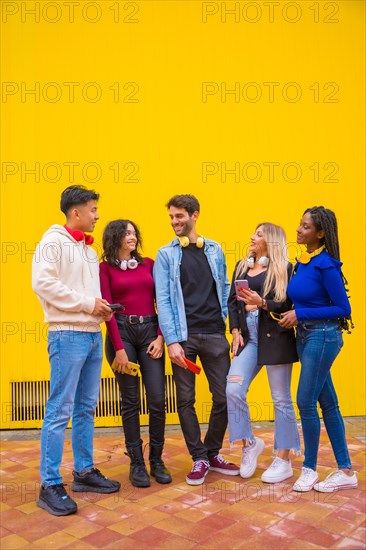 Portrait of a group of smiling young multi-ethnic teenage friends using cell phones on a yellow background