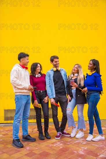 Portrait of a group of smiling young multi-ethnic teenage friends using cell phones on a yellow background