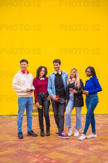 Portrait of a group of smiling young multi-ethnic teenage friends using cell phones on a yellow background