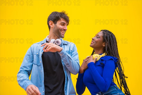 Multiethnic wedding couple of Caucasian man and woman of black ethnicity on a yellow background having fun