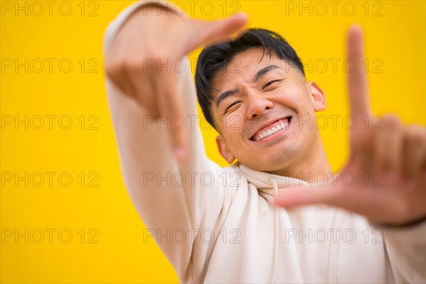 Portrait of south korean man in basic clothes over yellow background having fun and making take photo gesture