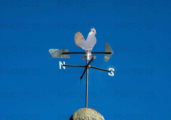 Weathercock in the shape of a rooster on a blue sky