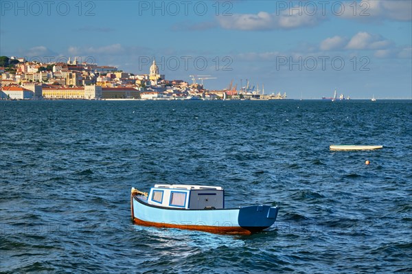 View of Lisbon over Tagus river from Almada with blue fishing boat and yachts tourist boats in background at sunset