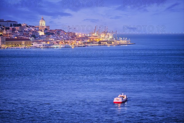 Night view of Lisbon over Tagus river from Almada with ferry and tourist boat in evening twilight