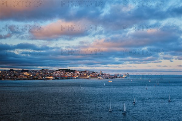 View of Lisbon over Tagus river from Almada with yachts tourist boats at sunset with dramatic sky