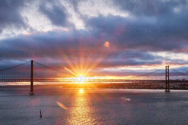 View of 25 de Abril Bridge famous tourist landmark of Lisbon connecting Lisboa and Almada on Setubal Peninsula over Tagus river with tourist yacht boats at sunset