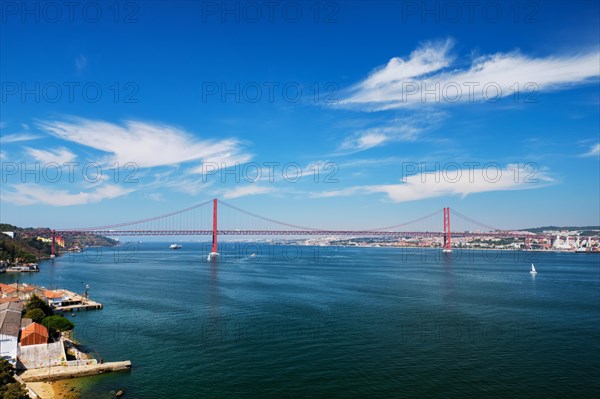 View of 25 de Abril Bridge famous tourist landmark of Lisbon connecting Lisboa to Almada on Setubal Peninsula over Tagus river with boats yachts and vessels