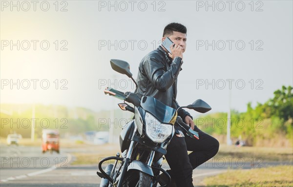 Biker sitting on motorcycle calling on the phone on the roadside