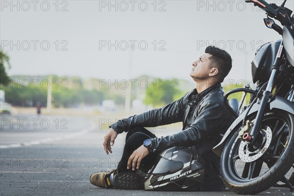 Male motorcyclist sitting and leaning on his motorcycle on the asphalt