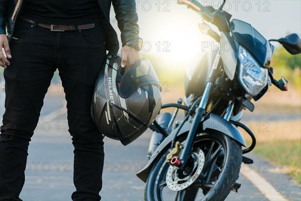 Unrecognizable biker holding helmet next to motorbike near the road