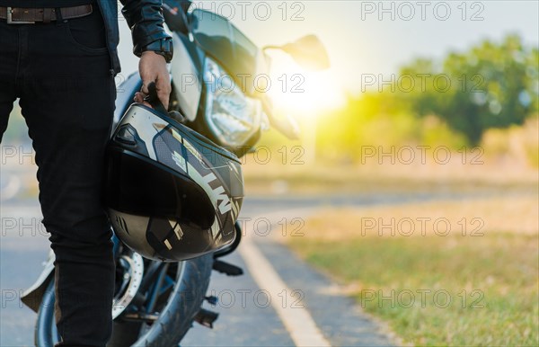 Motorcyclist holding safety helmet next to his motorbike near the road