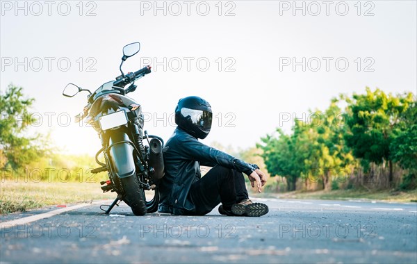 Male biker sitting next to his motorcycle on the road