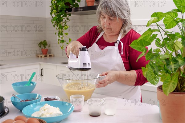 Woman chef in a white apron beating eggs in a bowl with an electric mixer to make a strawberry cake