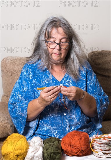 Front view of an older woman with white hair and glasses crocheting with her wool in the foreground