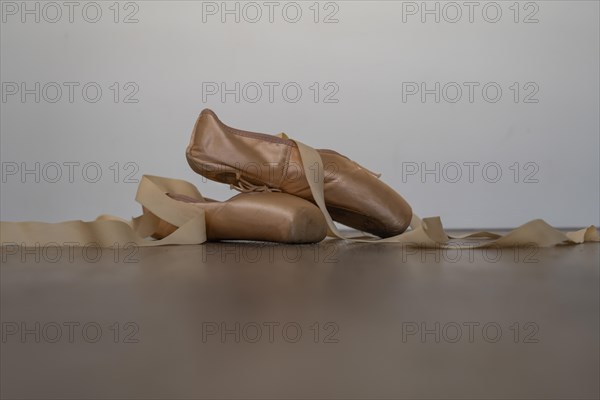 Ballet slippers with orange ribbon on a wooden floor and white background