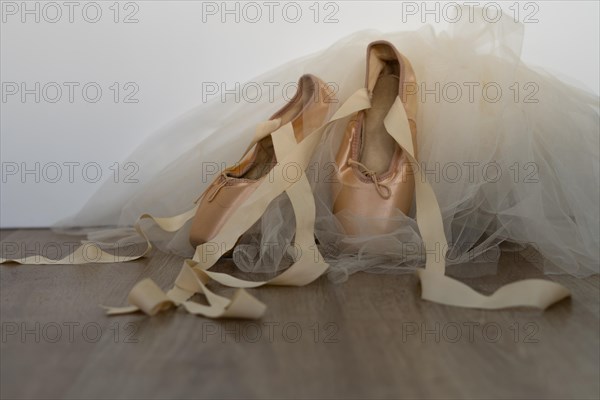 Ballet slippers with orange ribbon on a wooden floor and white background