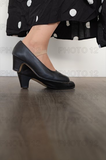 Legs of woman dancing flamenco with black clothes on wooden floor and white background