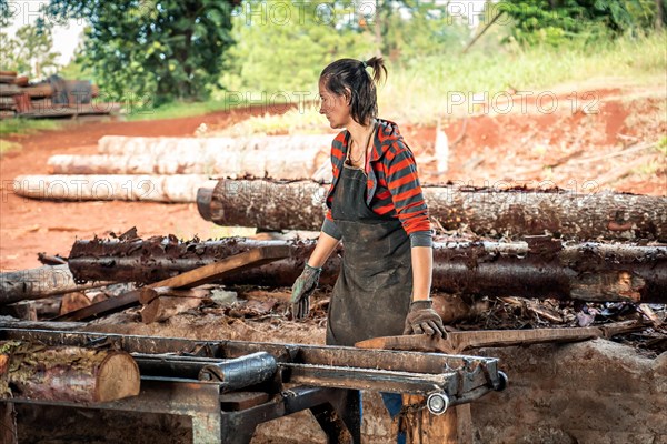 Woman in work clothes carrying a large log in a sawmill