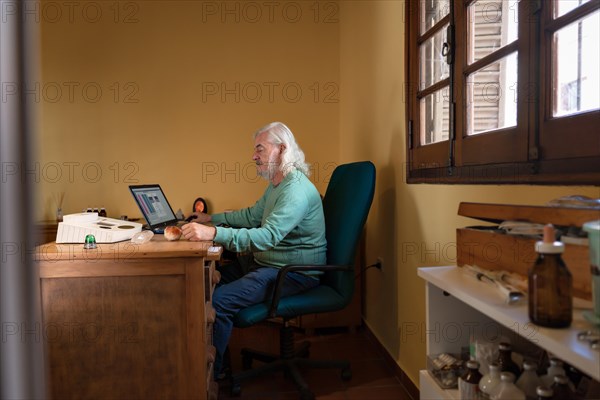 General shot of an elderly man sitting at his desk performing a quantum medicine analysis