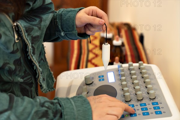 Close-up detail of a woman's hand holding a pendulum on a radionic machine