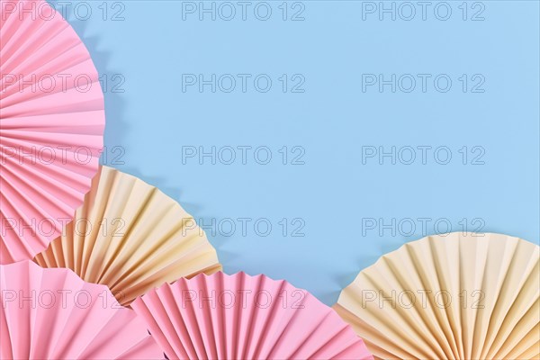Pink and beige paper craft rosettes on blue background with empty copy space in middle