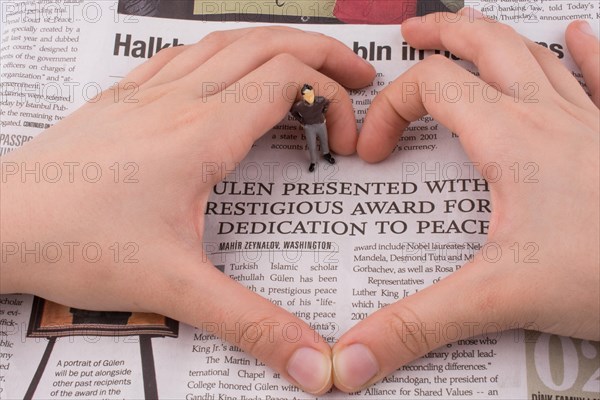 Human figure in the middle of a hand making a heart shape on a newspaper